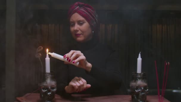 En spåman i en magisk salong tänder ljus på en svart bakgrund bakom magisk eld — Stockvideo