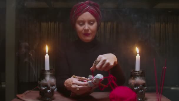 Ανώτερη μάγισσα γυναίκα μάντισσα χρησιμοποιεί βουντού κούκλα και κόκκινο σχοινί σε τρομερό μαγικό τελετουργικό — Αρχείο Βίντεο