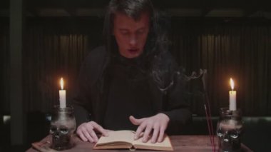 Yoğunlaşmış gizemli büyücü erkek falcı karanlık ofisinde büyü kitabı okuyor.