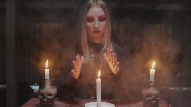 Junge Hexe Wahrsagerin bewegt ihre Hände über Kerze, schaltet sie aus und blickt in die Kamera — Stockvideo