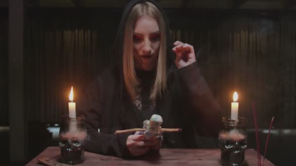 Ung häxa kvinnlig spåkvinna sätter en nål i voodoo docka i fruktansvärda magiska ritual — Stockvideo