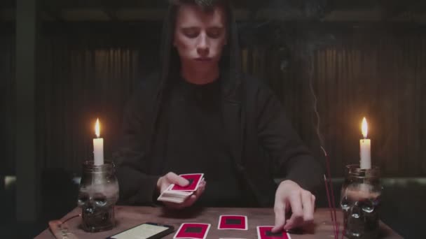 Skoncentrowany tajemniczy czarodziej męski wróżbita używa karty tarota i telefonu, aby odczytać przyszłość — Wideo stockowe