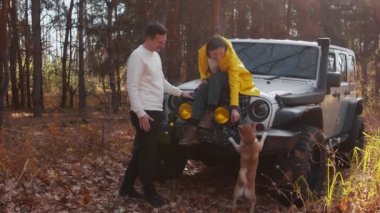 Sarı ceketli genç bir kadın arabasında oturuyor ve sonbahar ormanında köpeğini besliyor.