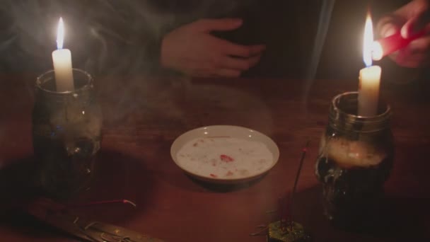 Крупним планом таємничий чарівник чоловічої статки запалює червону свічку і кладе її на тарілку в магічному ритуалі — стокове відео