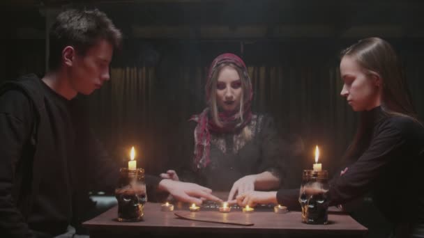 La adivina bruja trata de hablar con el fantasma. Dos mujeres y un hombre usan Ouija Juego de espíritu de mesa — Vídeo de stock