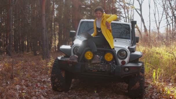 Joven mujer feliz en chaqueta amarilla se sienta en el coche y trabaja con el portátil y el teléfono en el bosque de otoño — Vídeos de Stock