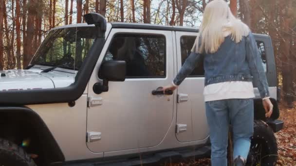Young blonde woman sits on the passenger seat in the car jeep in autumn forest — Stock Video