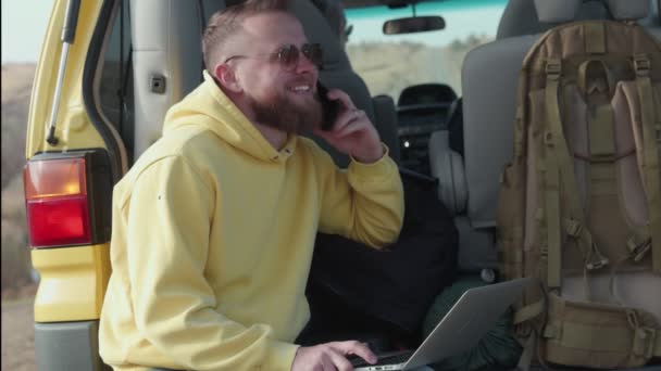 Щасливий бородатий чоловік позаштатний мандрівник говорить по телефону, сидячи в машині — стокове відео