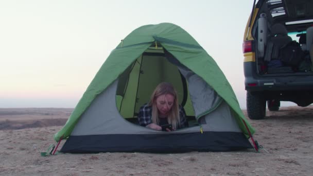 Jeune femme se couche dans la tente et utilise le téléphone sur la montagne — Video