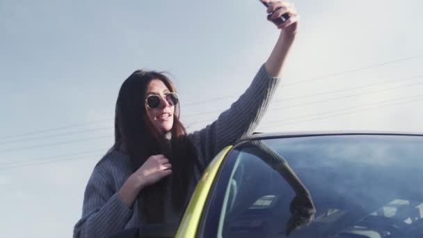 Young woman with sunglasses leaned out of the car window and records self video selfie stories — Stock Video