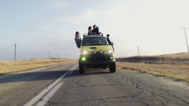 젊은 부부가 휴가철밴 지붕 위에 앉아 있고, 운전중에 선글라스를 쓴 젊은 여자가 앉아 있다 — 비디오