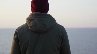 Yürüyüş hobisi. Kırmızı şapkalı sırt çantalı yalnız adam denize benziyor.