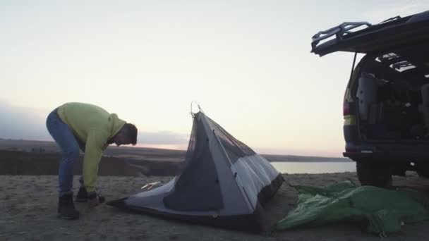 Młody człowiek w żółtej bluzie Rozbicie namiotu kempingowego — Wideo stockowe