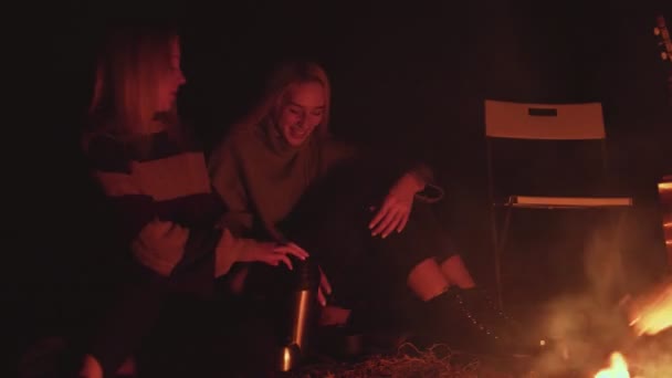 Piknik mladých lidí s ohněm v lese ve večerních hodinách. Veselí přátelé nalévá horký čaj v šálcích — Stock video