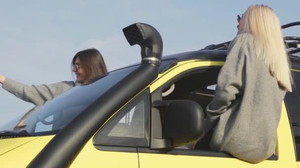 Dwie młode blondynki i brunetka w okularach przeciwsłonecznych wychylone przez okno samochodu i nagrywają własne filmy z selfie — Wideo stockowe