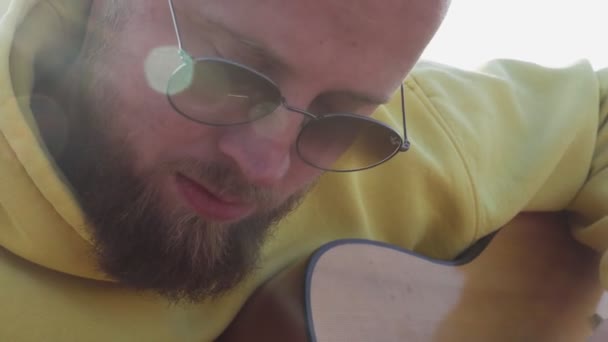 Młody hipster brodaty mężczyzna w okularach przeciwsłonecznych grać na gitarze na zewnątrz na kempingu — Wideo stockowe