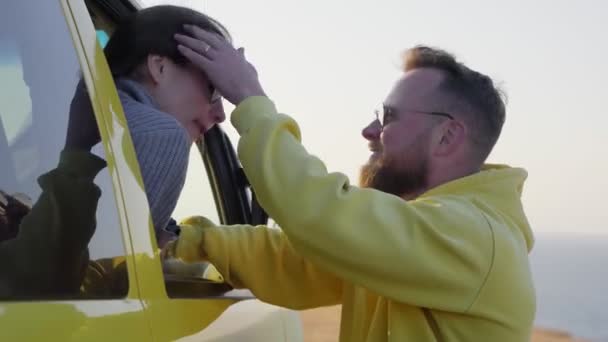 Szczęśliwy brodaty mężczyzna stoi w pobliżu samochodu, a jego dziewczyna siedzi w samochodzie i uśmiecha się do niego — Wideo stockowe