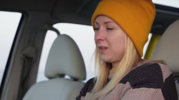 노란 모자를 쓴 젊은 여자가 차에 앉아 카메라 앞에 포즈를 취한다 — 비디오