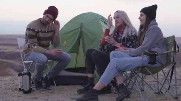 Jeunes amis heureux campeurs assis près de la tente et la voiture, boit un thé chaud et parle — Video