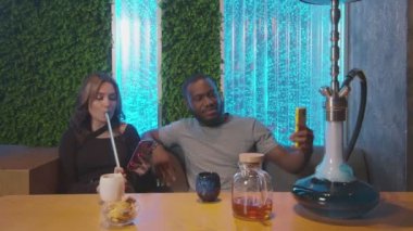 Genç Afrikalı bir adam sevgilisiyle selfie çekiyor, nargile içiyor.