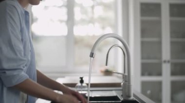 Lavaboda duran genç bir kadın mutfakta ellerini dikkatlice yıkıyor.