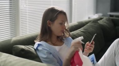 Genç bayan evi temizledikten sonra dinleniyor, kanepeye oturuyor ve telefon kullanıyor.