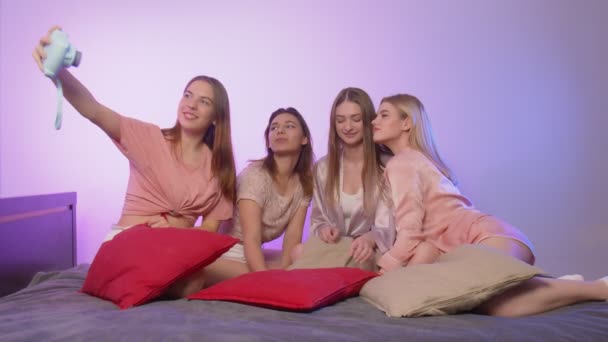 Dört mutlu, pijamalı genç kadın bekarlığa veda partisinde yatakta oturup klasik fotoğraf çekiyorlar. — Stok video