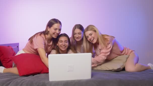 Four happy pretty young women in pajamas sits on bed and looks at the notebook at bachelorette party — Stock Video