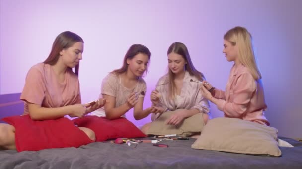 Quatro mulheres bonitas felizes no pijama senta-se na cama e fazer maquiagem na festa de despedida de solteira — Vídeo de Stock