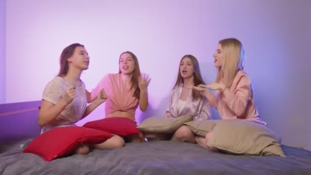 Four happy pretty young women in pajamas sits on bed and sings at bachelorette party — Stock Video