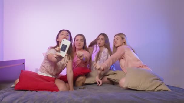 Four happy pretty young women in pajamas sits on bed, sings and records video on their phones at bachelorette party — Stock Video