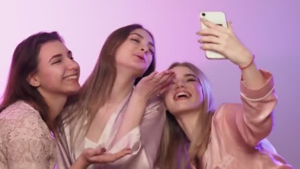 Quattro belle donne felici in pigiama si siedono sul letto e si fanno selfie al telefono all'addio al nubilato — Video Stock