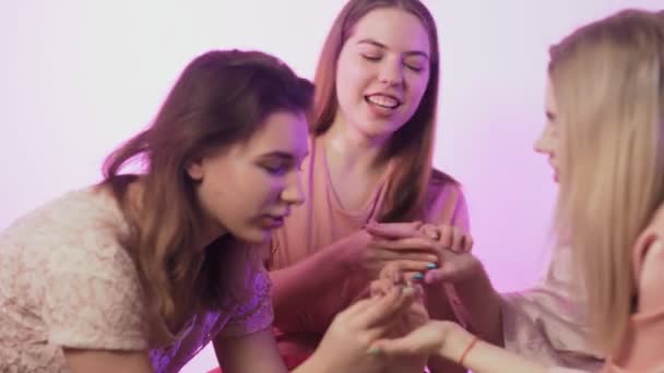 Four happy pretty young women in pajamas sits on bed and showing off their nails to each other at bachelorette party — Stock Video