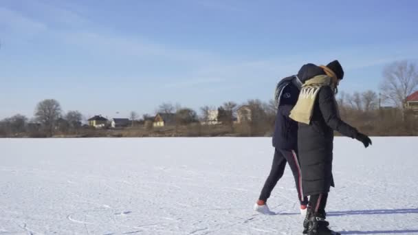 Mladý muž učí svou přítelkyni jezdit na bruslích na zamrzlém jezeře v lese — Stock video