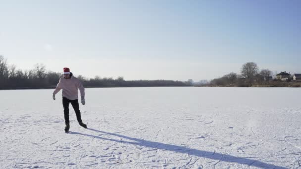Mladý muž v vánoční Santa klobouk jezdí bruslení na zamrzlé jezero v lese — Stock video