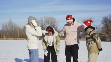Noel Baba şapkalı dört arkadaş, ormanda büyük donmuş bir gölde buz pateni yaptıktan sonra kameraya poz veriyor.
