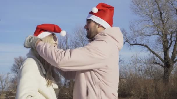 Jeune homme met un chapeau de Noël sur sa petite amie à l'extérieur — Video