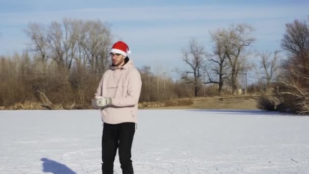 Młody człowiek w świątecznym kapeluszu jeździ na łyżwach i robi sobie selfie przez telefon na zamarzniętym jeziorze w lesie — Wideo stockowe