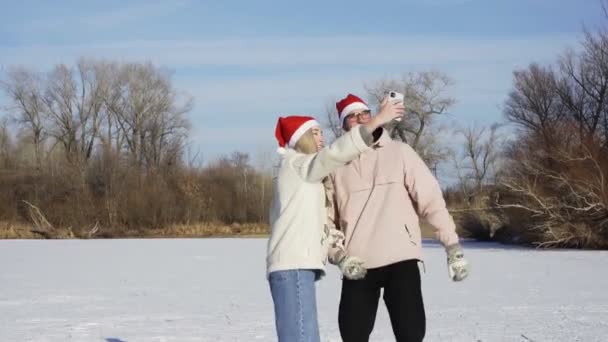 Młoda para w Boże Narodzenie Santa kapelusze jeździ na łyżwach i robi selfie na telefon na zamarzniętym jeziorze w lesie — Wideo stockowe