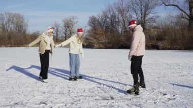 Noel Baba şapkalı genç adam ormandaki donmuş gölde telefonla kız arkadaşlarının fotoğrafını çekiyor.