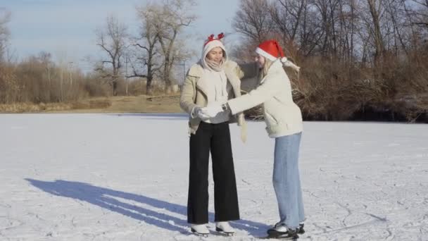 Dvě mladé ženy v vánoční klobouky jezdí bruslení a pády na ledě — Stock video