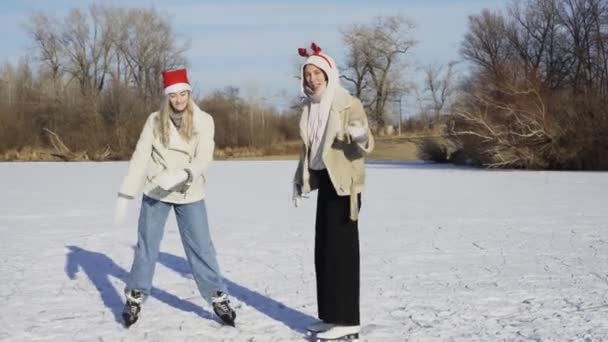 Dvě mladé ženy v vánoční klobouky jezdí bruslení a pády na ledě — Stock video