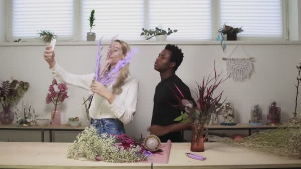 Junges Paar Geschäftspartner in ihrem Blumenladen. Junge Floristin macht Selfie am Telefon — Stockvideo