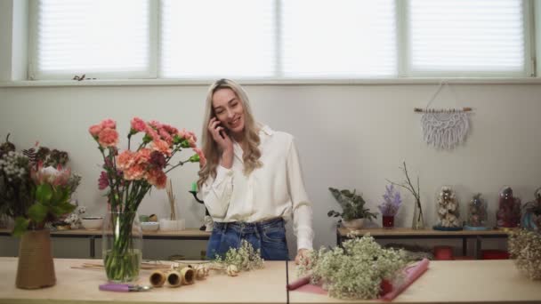 Ung munter kvinde blomsterhandlere taler til kunden via telefon i blomster butik – Stock-video