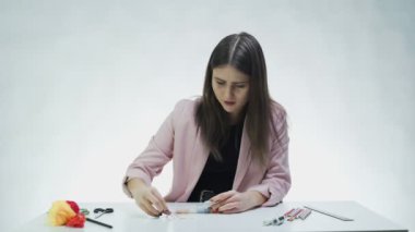 Çekici genç bir kadın beyaz bir stüdyoda masanın üstündeki kutulardan boncukları çıkarır.