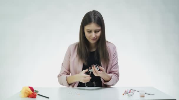 Une jeune femme séduisante déroule une ligne métallique et perle à la table dans un studio blanc — Video