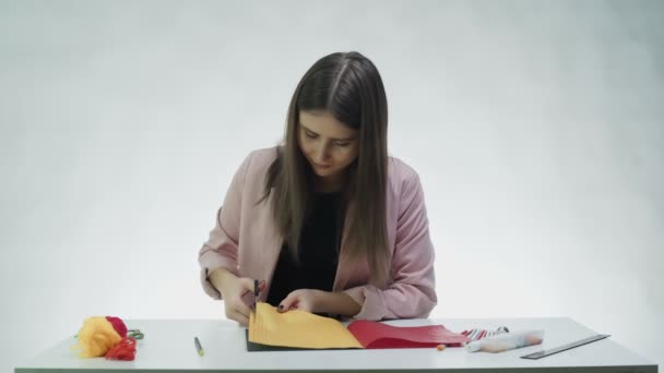 Mujer joven atractiva utiliza tijeras para cortar líneas de papel de color en la mesa en un estudio blanco — Vídeo de stock