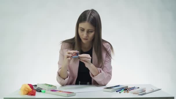 Atractiva joven utiliza pastel para dibujar algo en un papel blanco en la mesa en un estudio blanco — Vídeo de stock