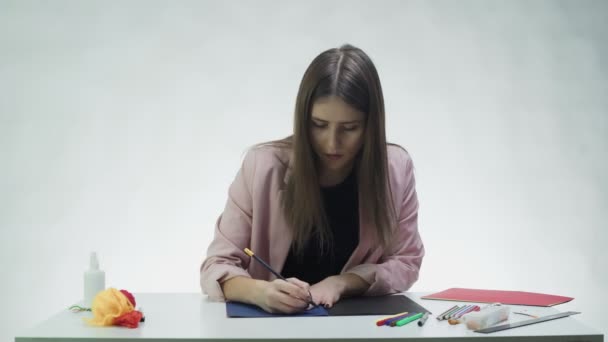Atraktivní mladá žena kreslí akrylovými barvami na bílém papíru u stolu v bílém studiu — Stock video
