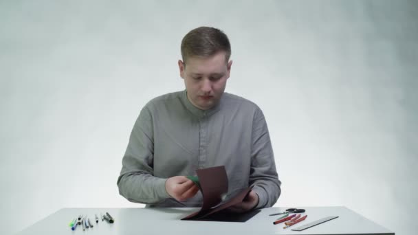 Młody człowiek używa ołówka i linijki do rysowania linii na zielonym papierze przy stole w białym studiu — Wideo stockowe